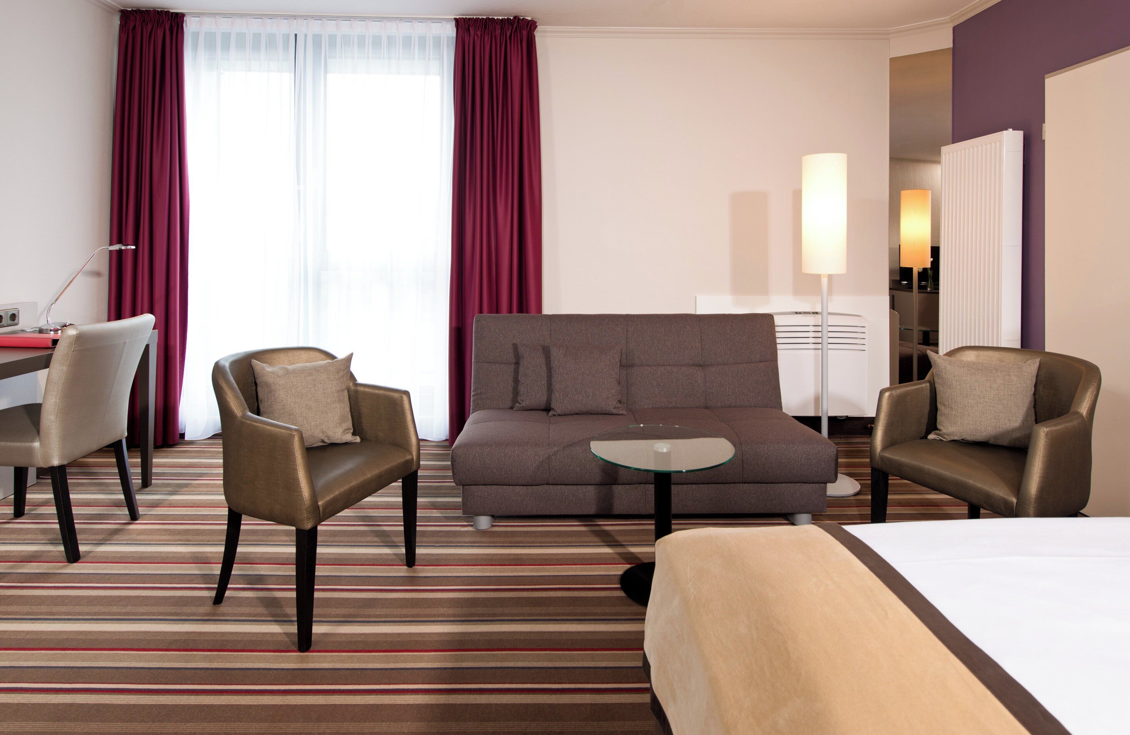 A hotel room with a bed, two armchairs, a sofa, a small table, and a desk with a lamp.