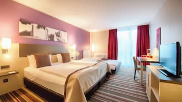 Habitación de hotel con dos camas, un escritorio con televisor y un ventanal con cortinas rojas.