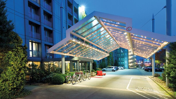 A modern hotel entrance with a glass canopy, a bike parking area, and a clear view of the building's exterior.