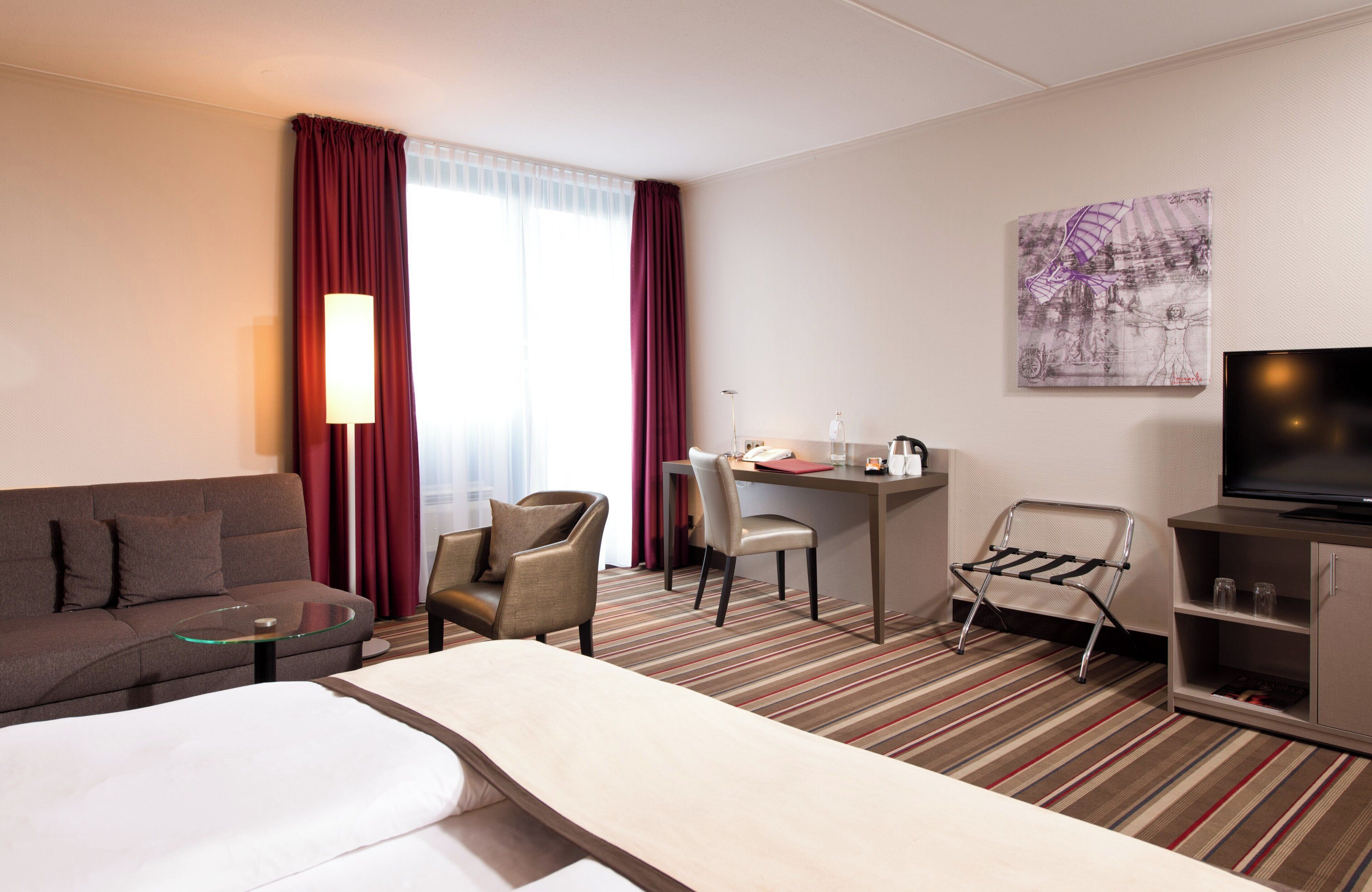 Une chambre d’hôtel avec un canapé, un lit, un bureau avec une chaise, une télévision et un tableau au mur.
