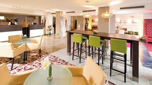 A hotel lobby with a reception desk, seating area with round tables, and a bar with high stools.