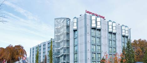 Un hotel moderno con fachada de vidrio, varios pisos y un llamativo letrero que dice 'Leonardo Hotel'.