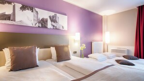 A hotel room with two beds, a headboard, wall-mounted artwork, and a vase with flowers.