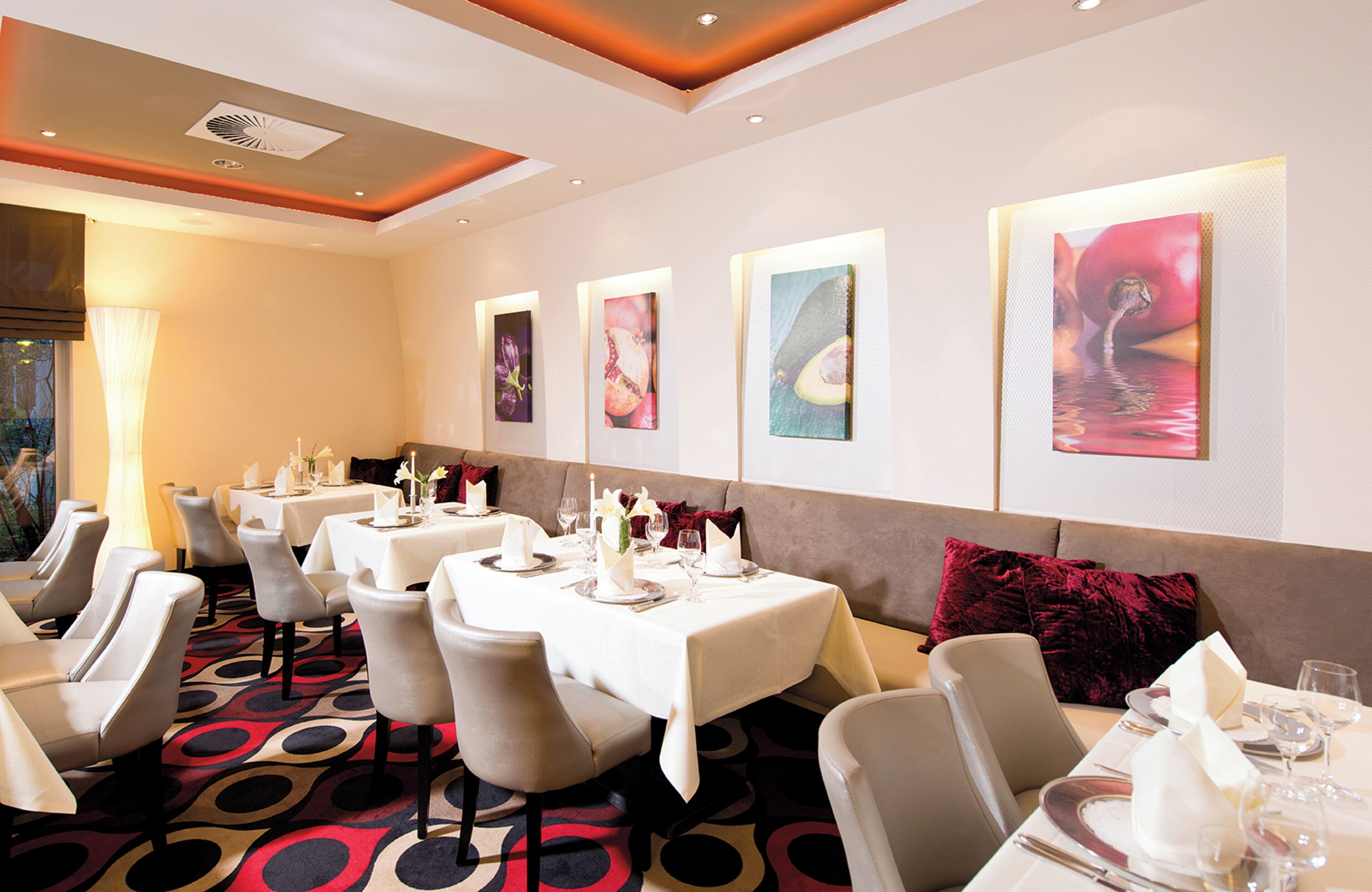 A dining area with tables set for a meal, featuring artwork on the walls and a patterned carpet.