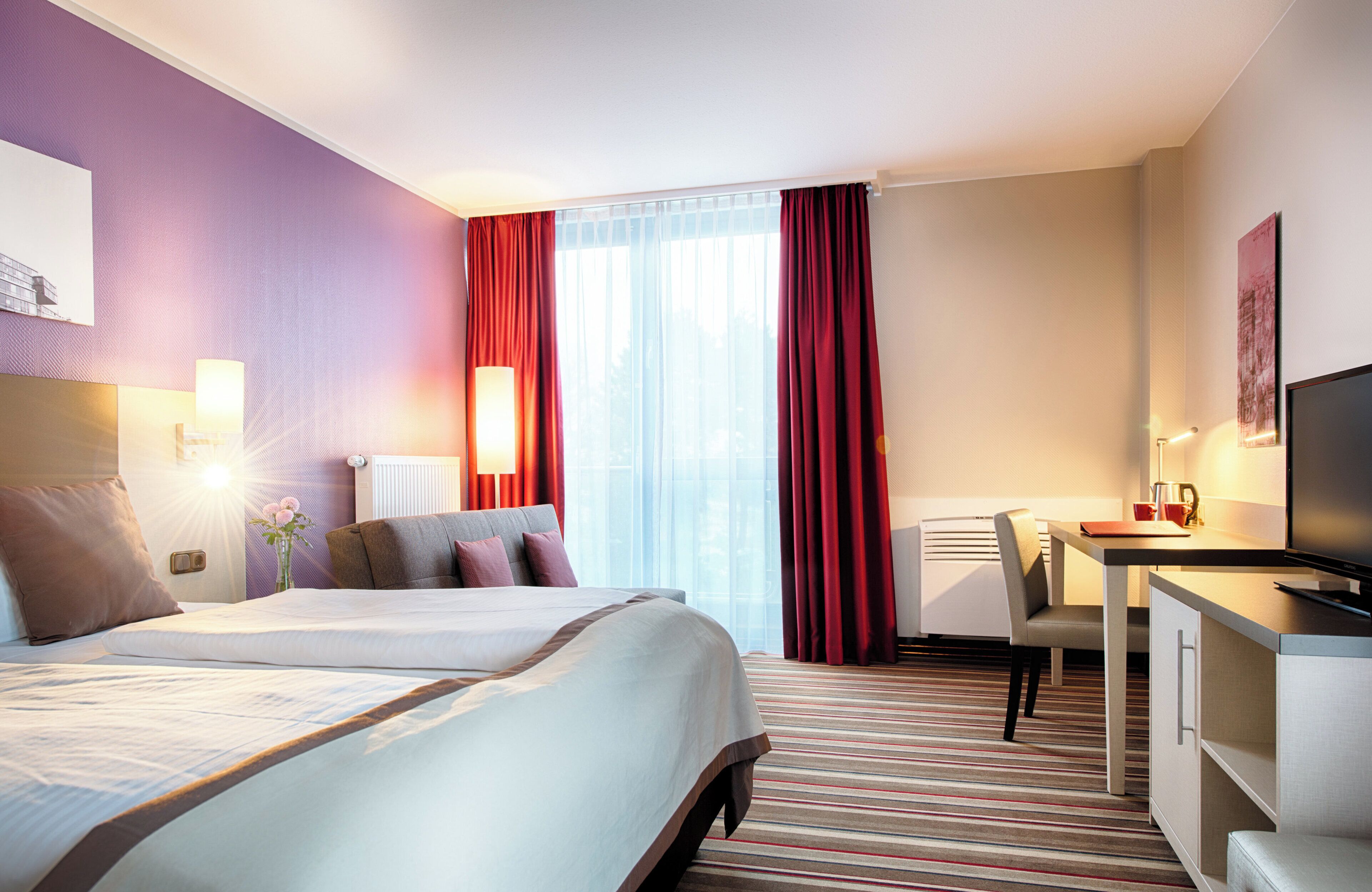 A hotel room with a large bed, a desk, a chair, and a television.