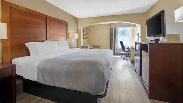 A hotel room with a large bed, a desk with a computer, a television, and a window with curtains. - Quality Inn Fuquay Varina East (Fuquay-Varina)