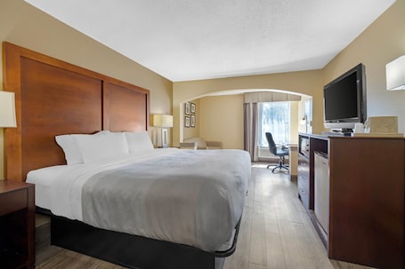 A hotel room with a large bed, a desk with a computer, a television, and a window with curtains.. Quality Inn Fuquay Varina East
