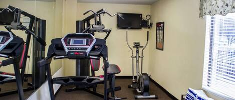 Un gimnasio con cintas de correr, elíptica, bicicleta estática y una televisión en la pared.