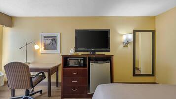 A hotel room with a bed, a desk with a chair, a television, a microwave, a refrigerator, a lamp, and a mirror.