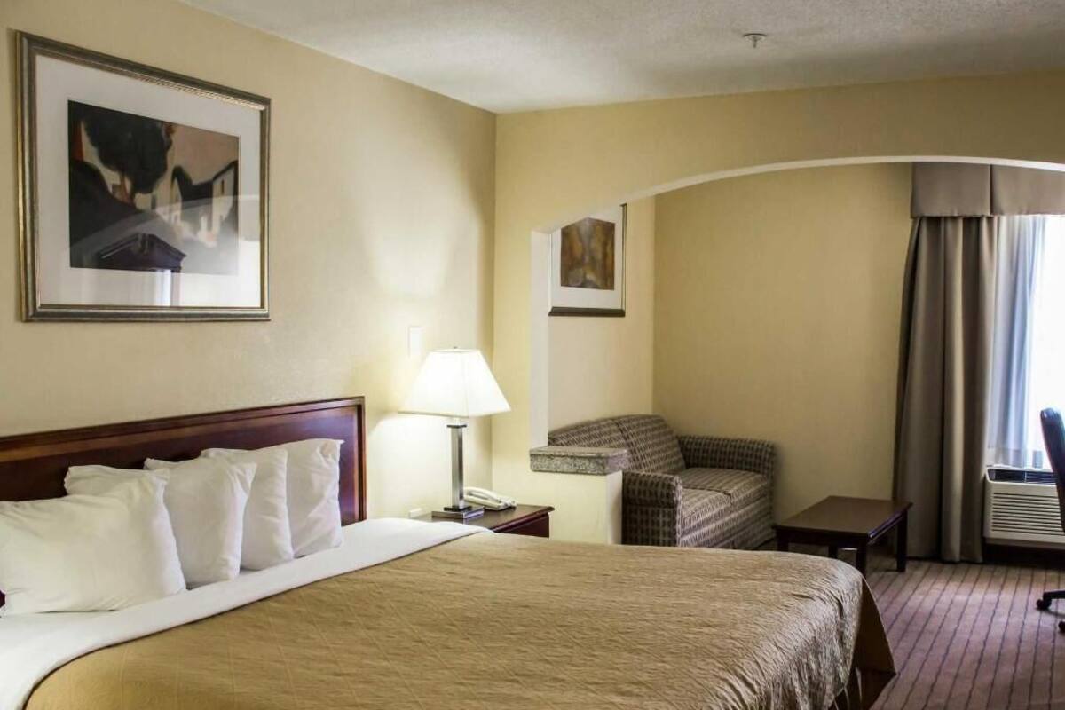 A hotel room with a large bed, a chair, a desk, and a lamp.