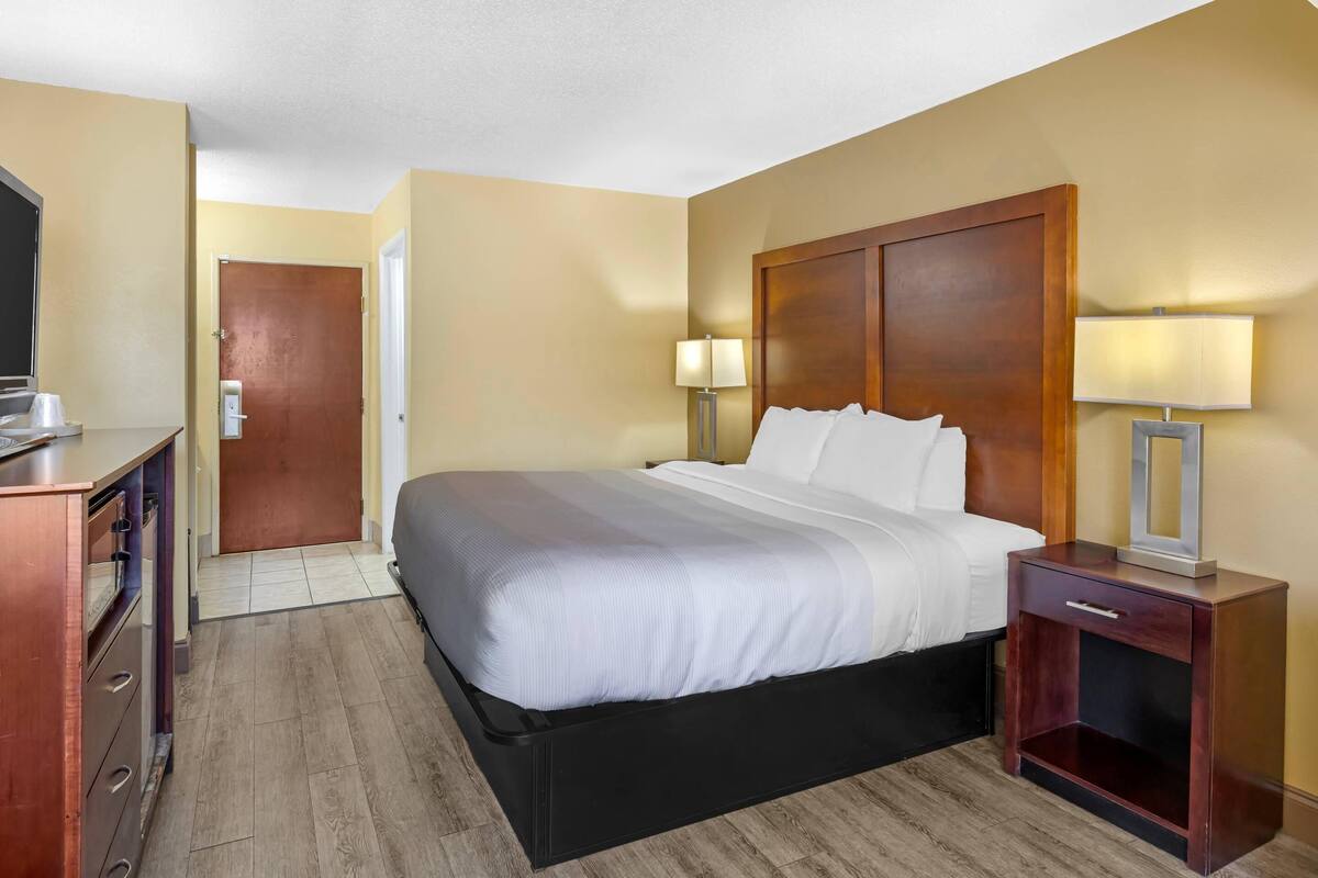 A hotel room with a bed, bedside table, lamp, and a door leading to another room.