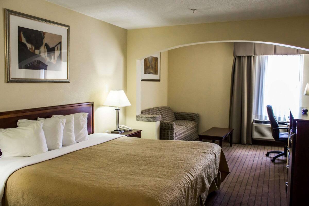 A hotel room with a large bed, a desk, a chair, and a lamp.