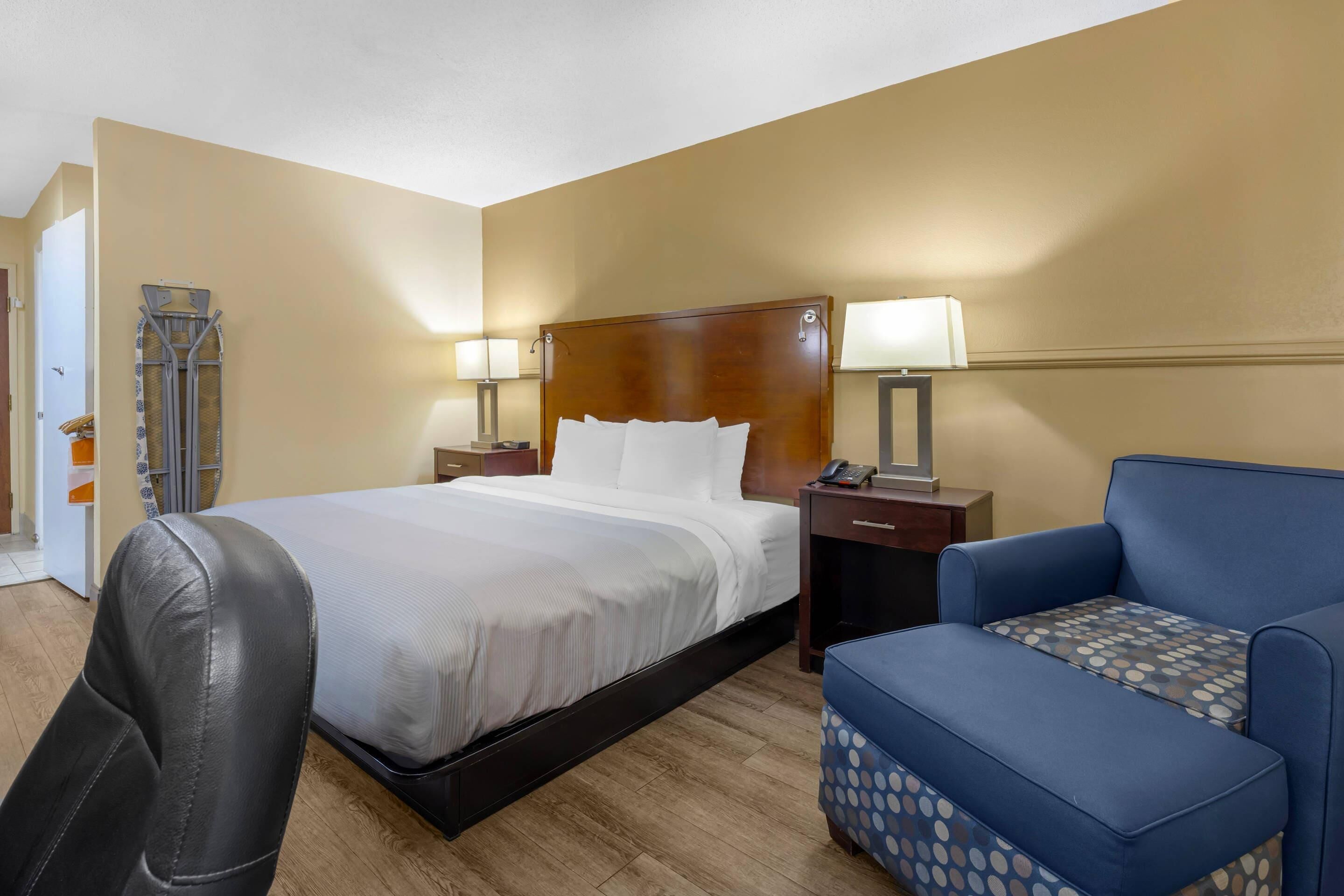 A hotel room with a bed, a chair, a nightstand, and a lamp.