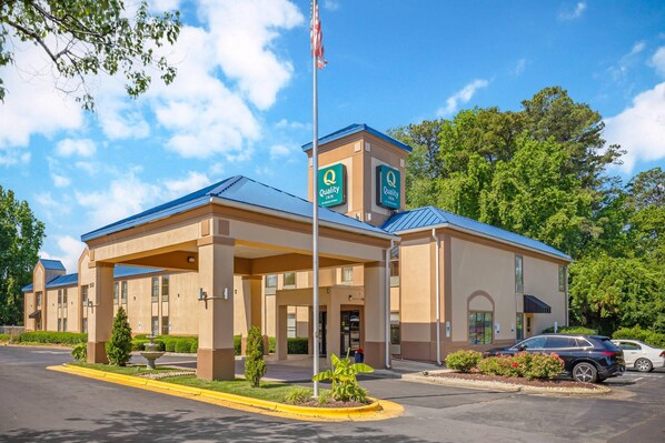 A hotel with a covered entrance, a flagpole with an American flag, and a parking lot with cars.