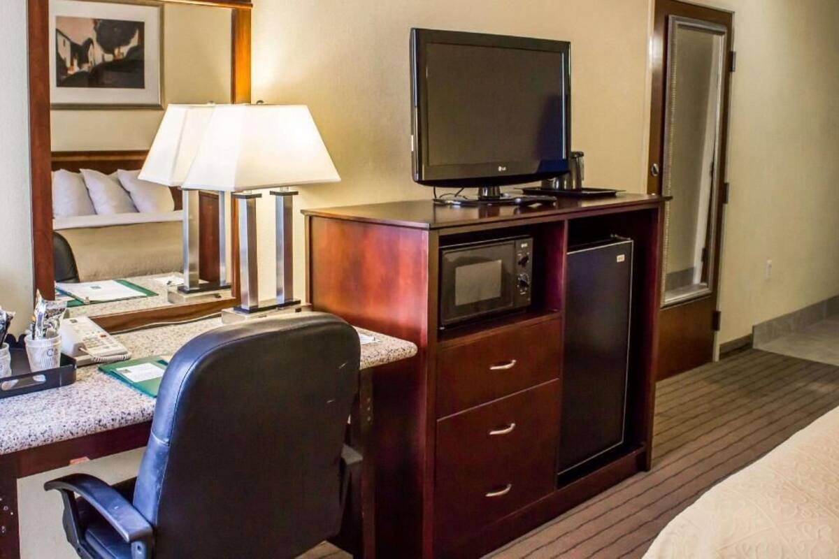 A hotel room with a bed, desk, chair, television, microwave, and a small refrigerator.