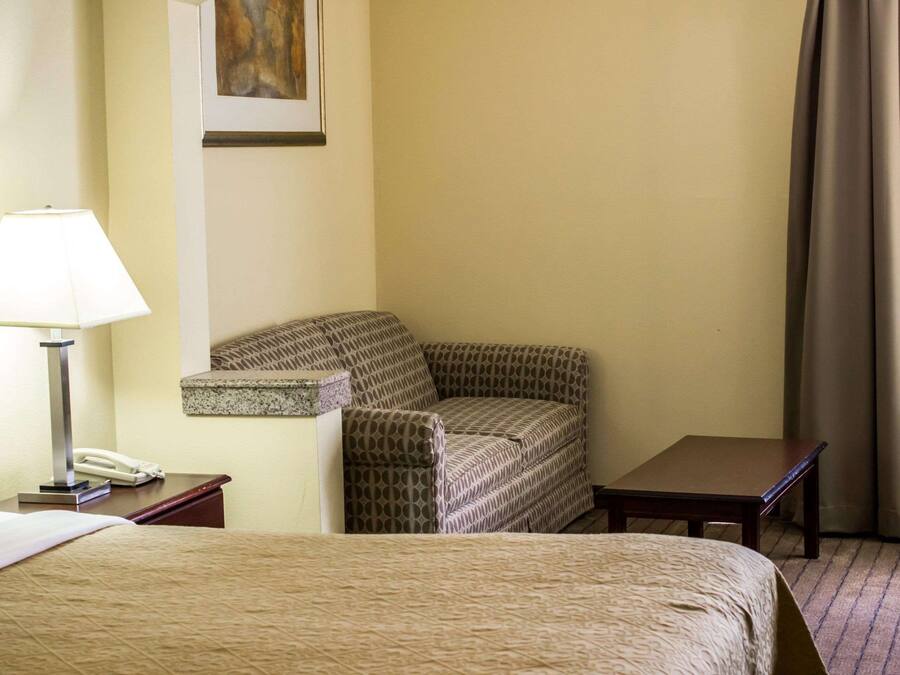 A hotel room with a bed, a chair, a small table, a lamp, and a phone on a nightstand.