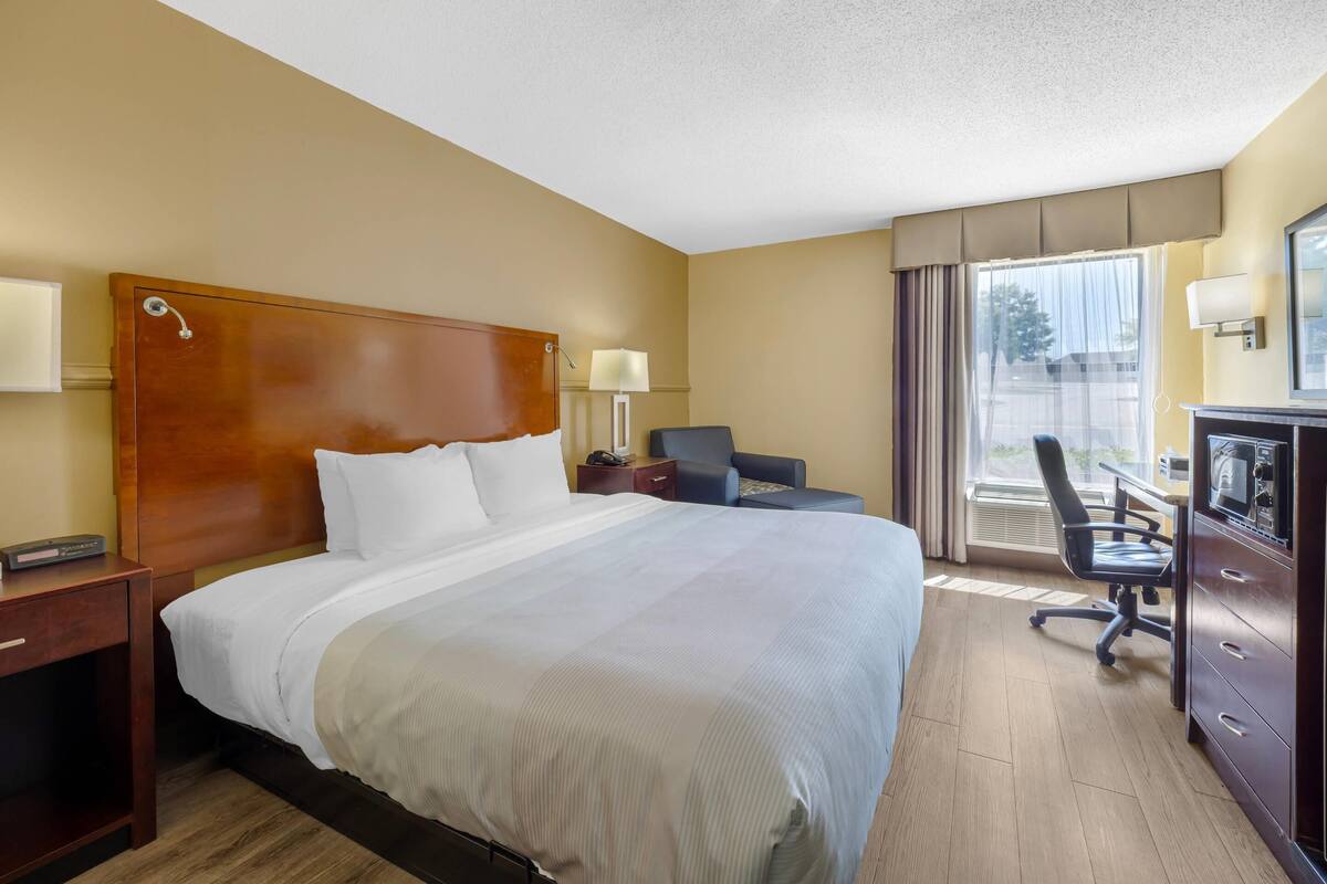 A hotel room with a large bed, a desk with a chair, a television, and a window with curtains.