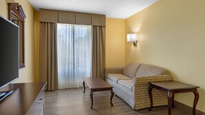 A hotel room with a sofa, a small table, a TV, and a window with curtains. - Quality Inn Fuquay Varina East (Fuquay-Varina)