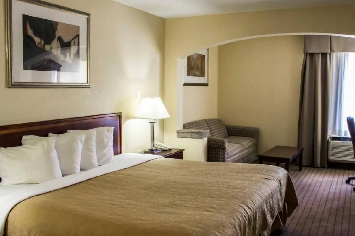 A hotel room with a large bed, a chair, a desk, and a lamp.