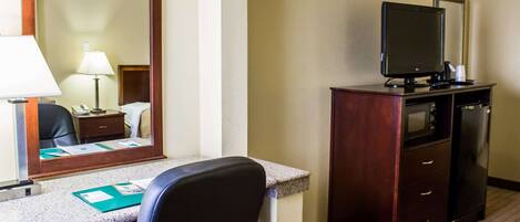 A hotel room with a desk, chair, mirror, television, and a small cabinet.