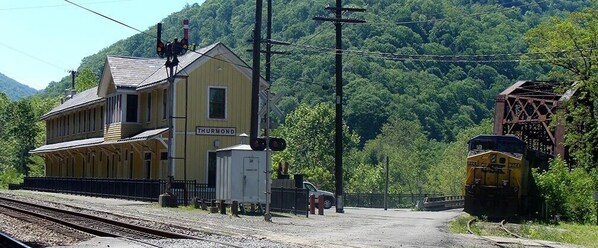 Una estación de tren llamada Thurgood, con un edificio amarillo, vías y un tren.