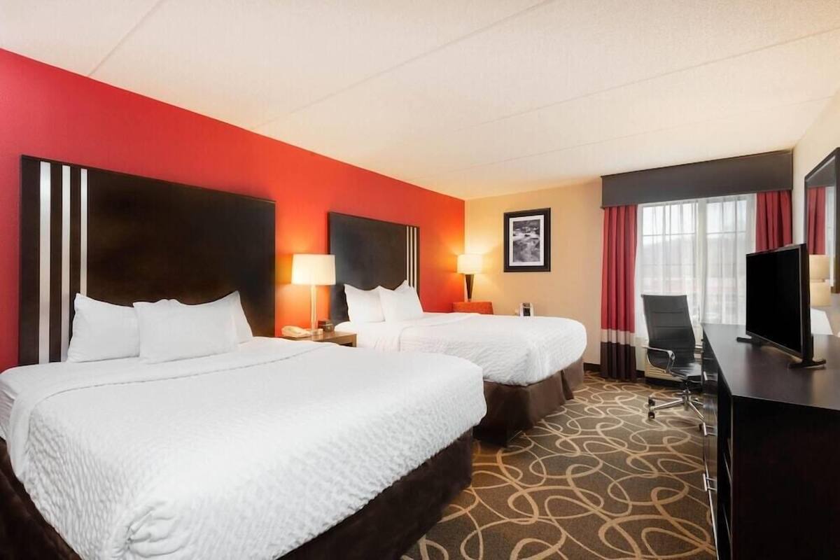 Een hotelkamer met twee bedden, een bureau, een televisie en een raam met gordijnen.