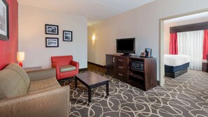 Una habitación de hotel con sofá, un sillón rojo, televisión, armario y cama.