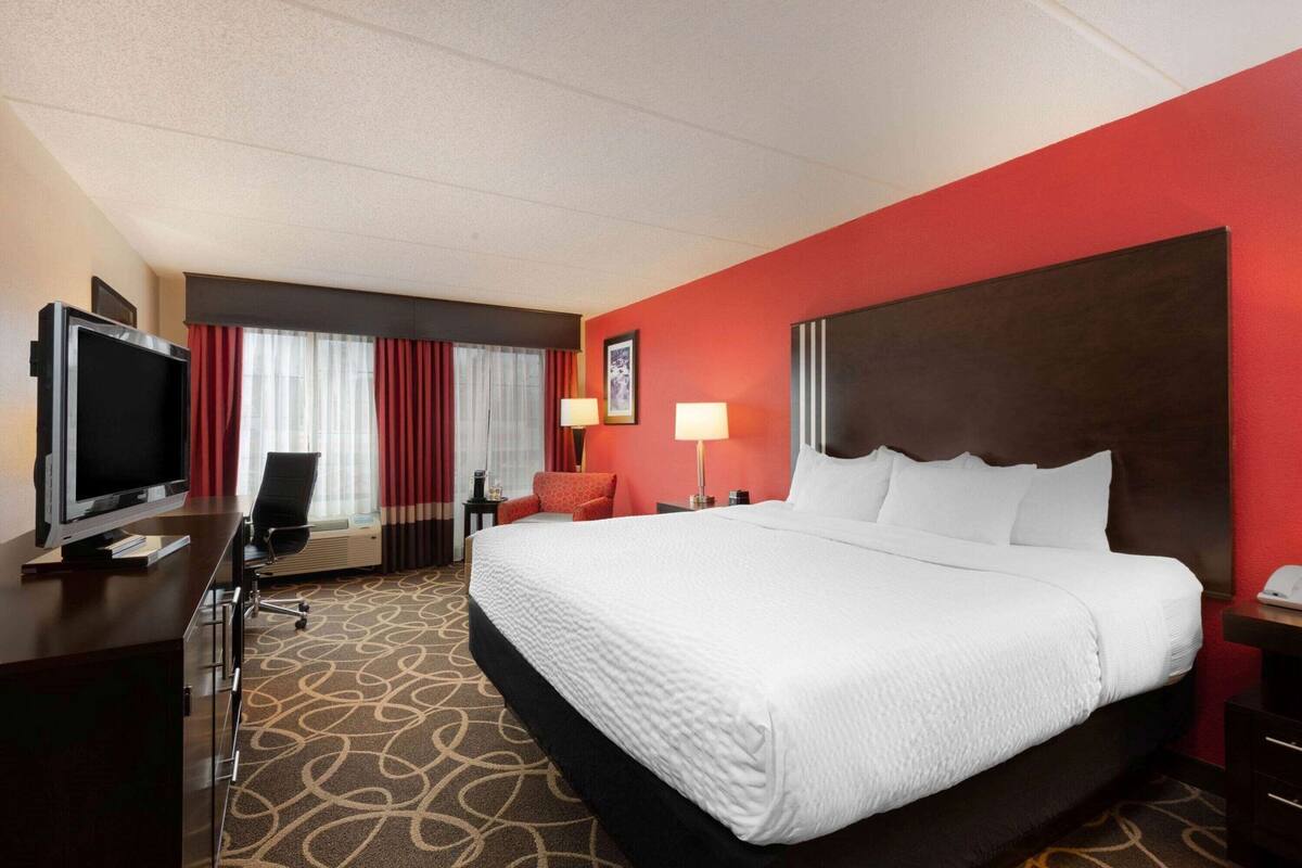 Hotelkamer met een groot bed, een bureau met televisie, een stoel, een lamp en een raam met gordijnen.