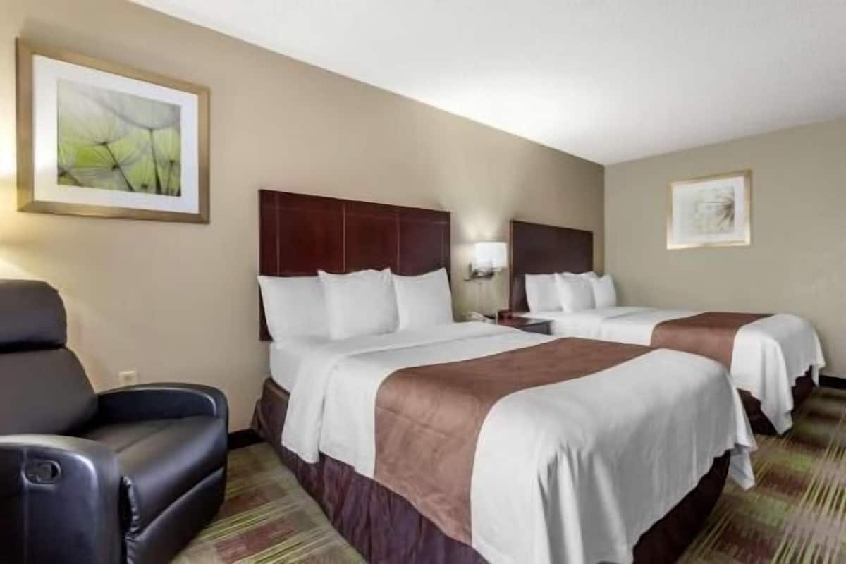 A hotel room with two beds, a chair, and artwork on the walls.