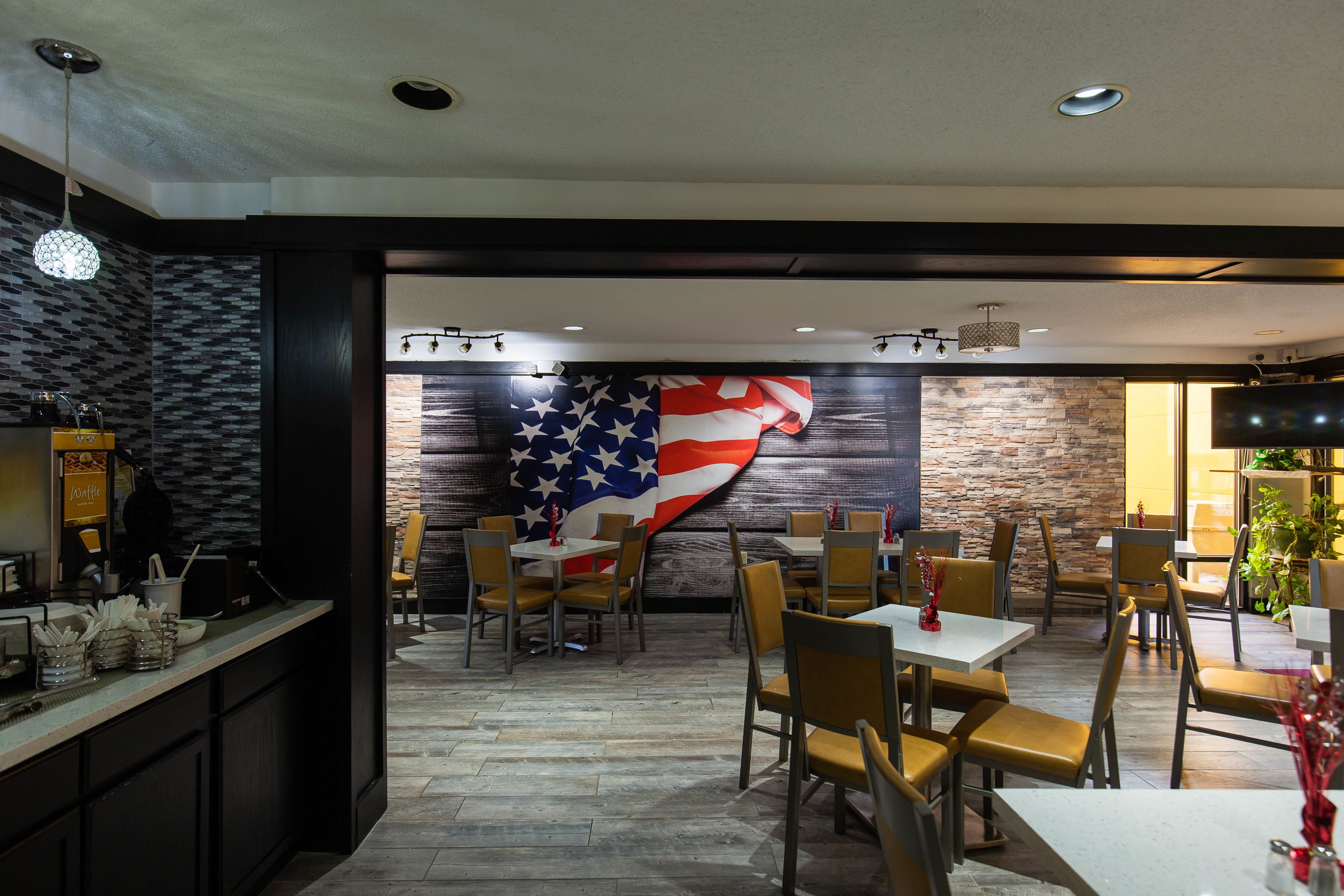 A restaurant with a large American flag mural on the wall, wooden flooring, and a mix of table and booth seating.