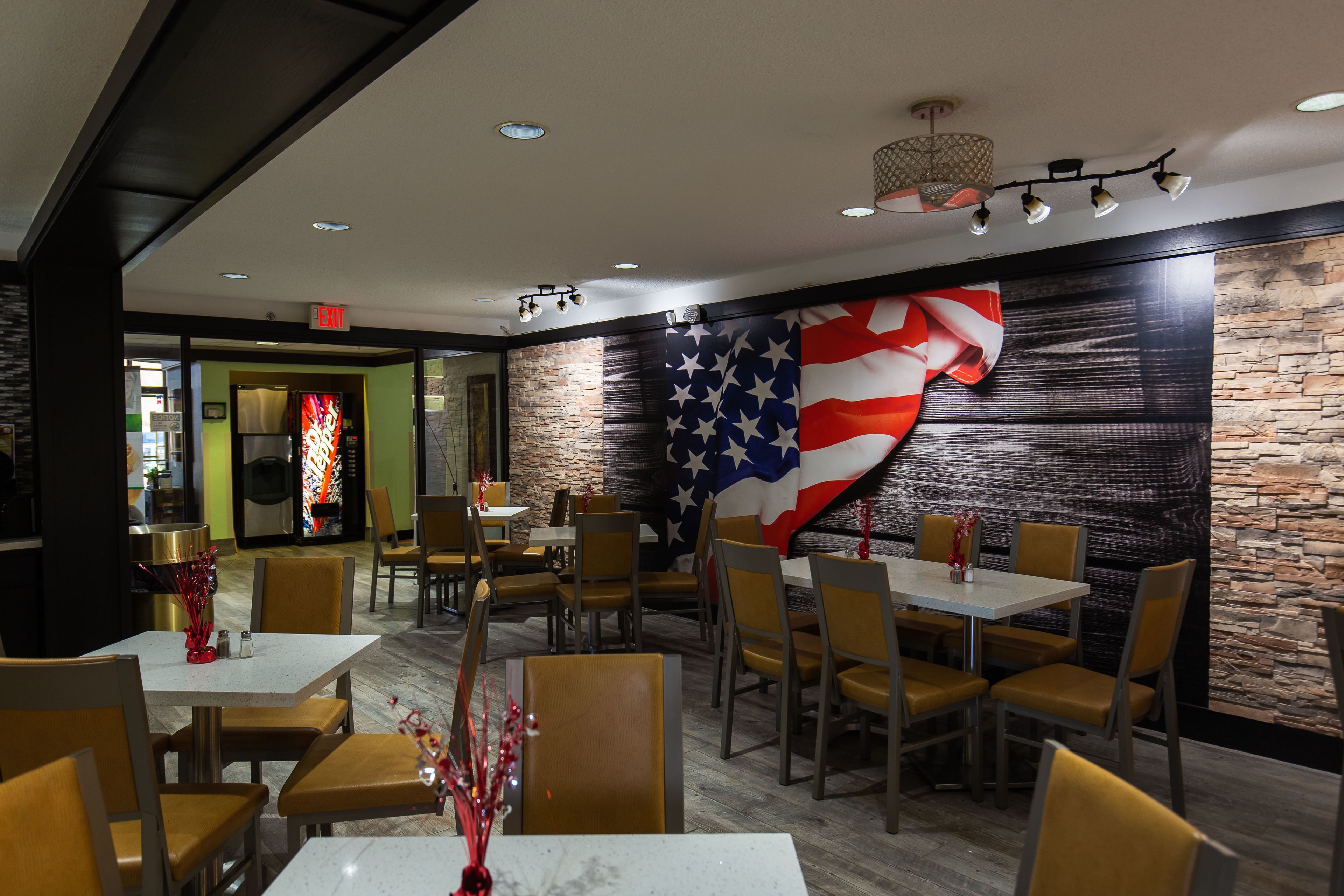 A restaurant interior with tables and chairs, a large American flag on the wall, and a stone accent wall.