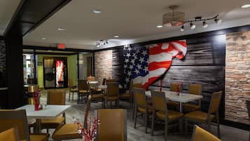A restaurant interior with tables and chairs, a large American flag on the wall, and a stone accent wall.