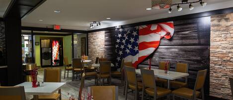 A restaurant interior with tables and chairs, a large American flag on the wall, and a stone accent wall.