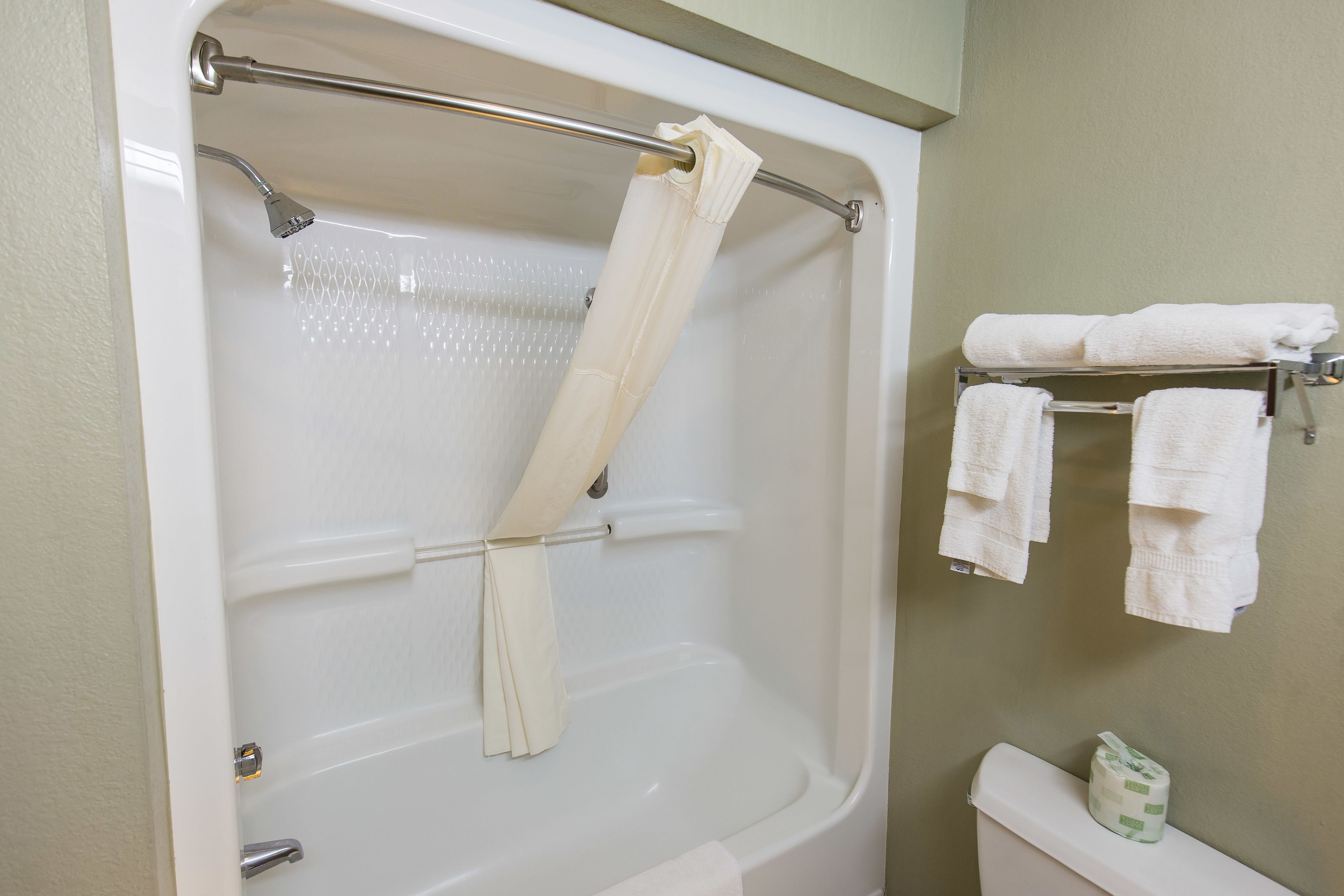 A bathroom with a bathtub, a shower curtain, a towel rack with towels, and a toilet.