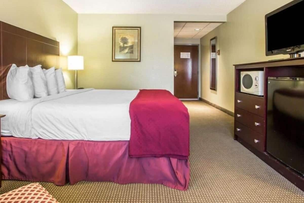 A hotel room with a bed, a television, a dresser, and a door leading to another room.