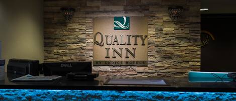 A reception desk with a sign for Quality Inn by Choice Hotels, a stone wall, and a blue-lit aquarium.