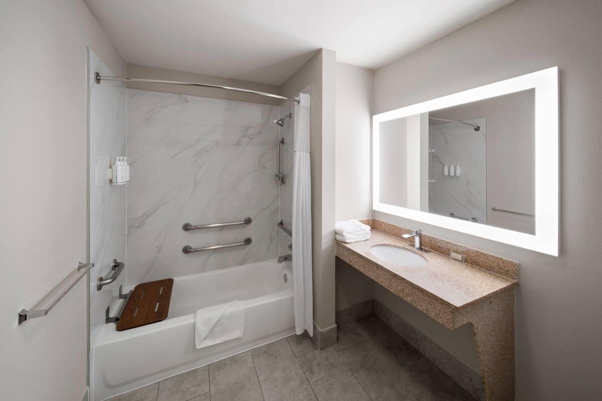 Une salle de bain moderne dotée d’une douche à parois de verre, d’une baignoire sur pieds, d’un lavabo en granit et d’un grand miroir.