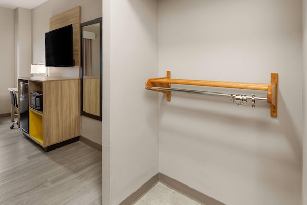 A hotel room with a wooden desk, a flat-screen TV, a mirror, and a towel rack.