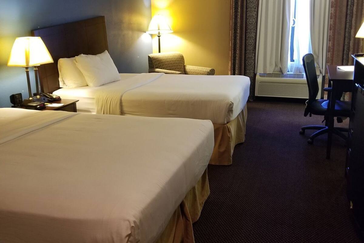 Une chambre d’hôtel avec deux lits, un bureau, une chaise et une lampe.