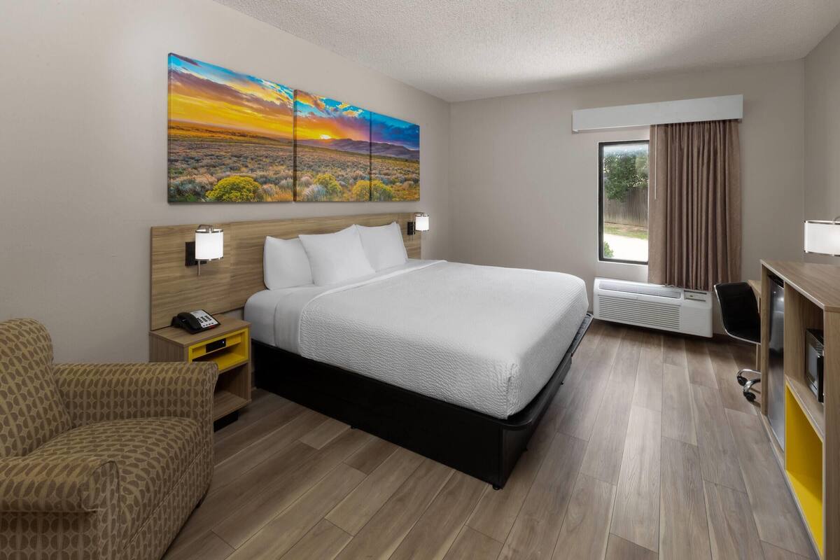 Une chambre d’hôtel avec un grand lit, un bureau, une chaise, un tableau et une fenêtre avec des rideaux.
