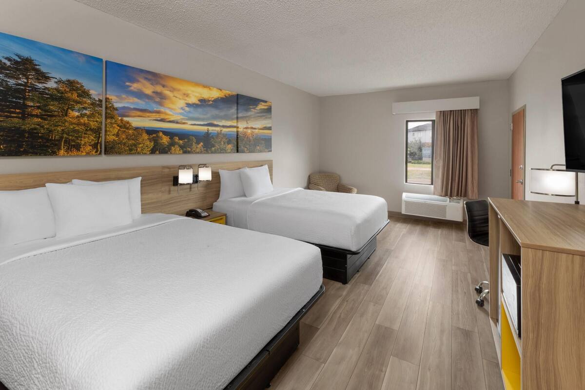 Une chambre d’hôtel avec deux lits, un bureau, une chaise, une télévision et une grande fenêtre avec des rideaux.