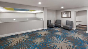 Une chambre d’hôtel avec un grand lit, un coin salon avec deux fauteuils, un miroir au mur et une moquette à motifs.