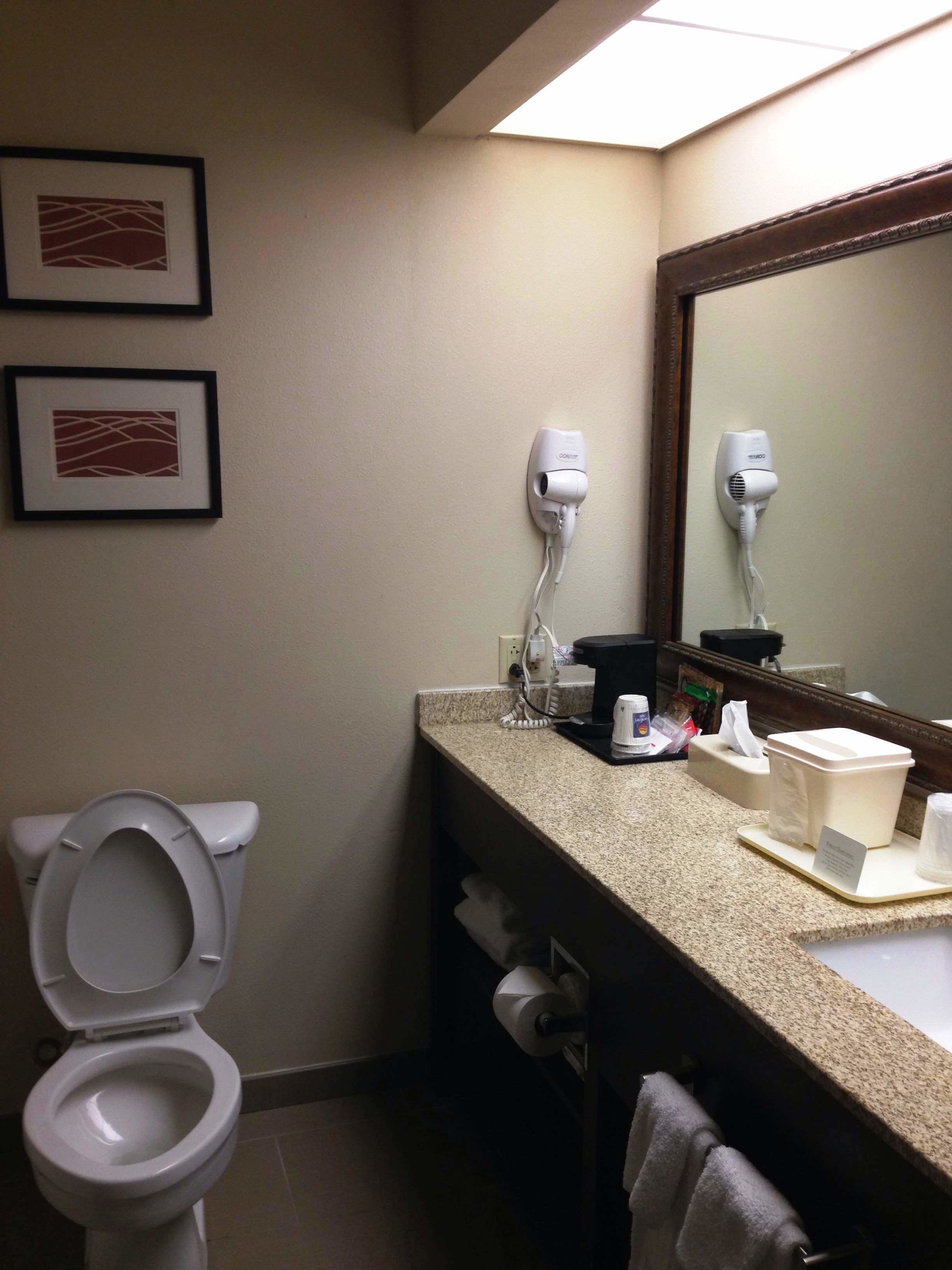 A bathroom with a toilet, a sink with a mirror, and two hair dryers mounted on the wall.