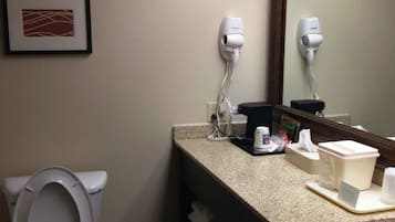 A bathroom with a toilet, a sink with a mirror, and two hair dryers mounted on the wall.