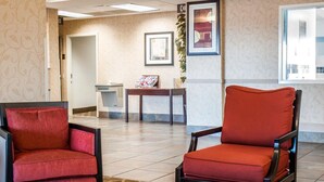 A hotel lobby with a reception desk, two red chairs, a patterned rug, and framed artwork on the walls.