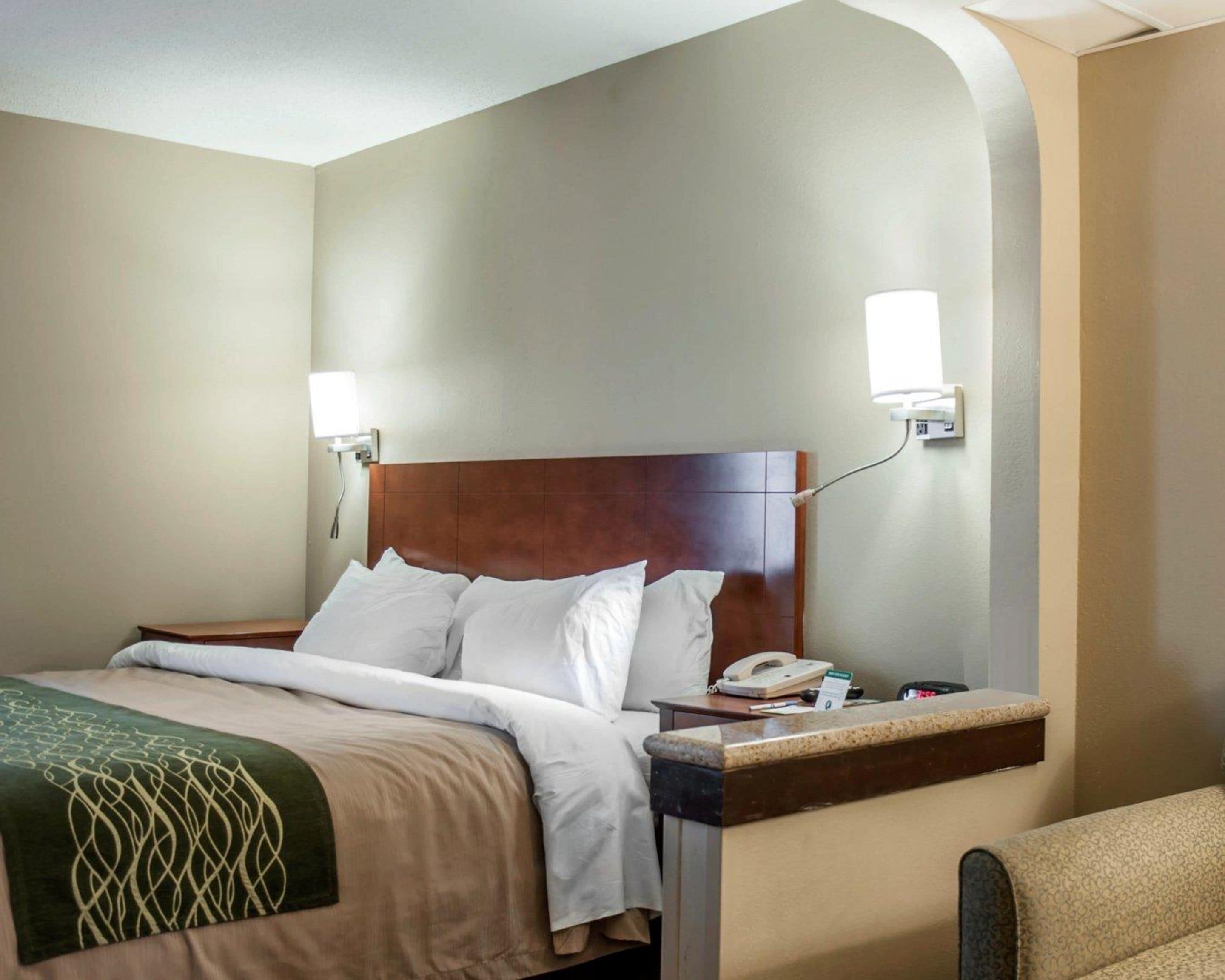Una habitación de hotel con cama, mesita de noche, lámpara y teléfono.