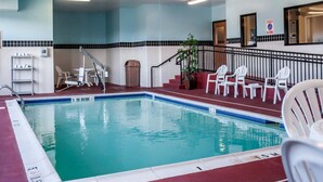 An indoor swimming pool with a blue and white tiled floor, a red border, and a staircase leading to a balcony with white chairs.