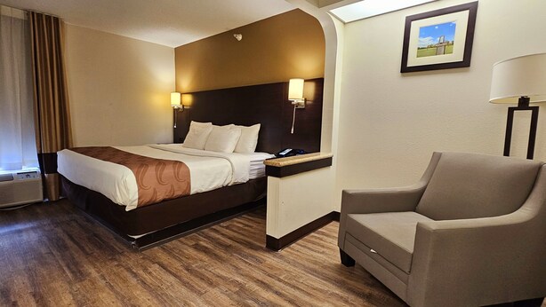A hotel room with a bed, a chair, a nightstand, and a picture on the wall.