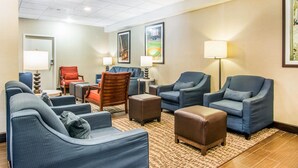A hotel lobby with multiple seating areas, including sofas and armchairs, arranged around a central coffee table. There are framed pictures on the walls, and a lamp is visible on the right side. - Comfort Inn Atlanta Downtown South (Atlanta)