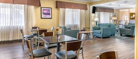 Zona pranzo di un hotel con un tavolo e sedie in legno, un divano e una TV montata a parete.